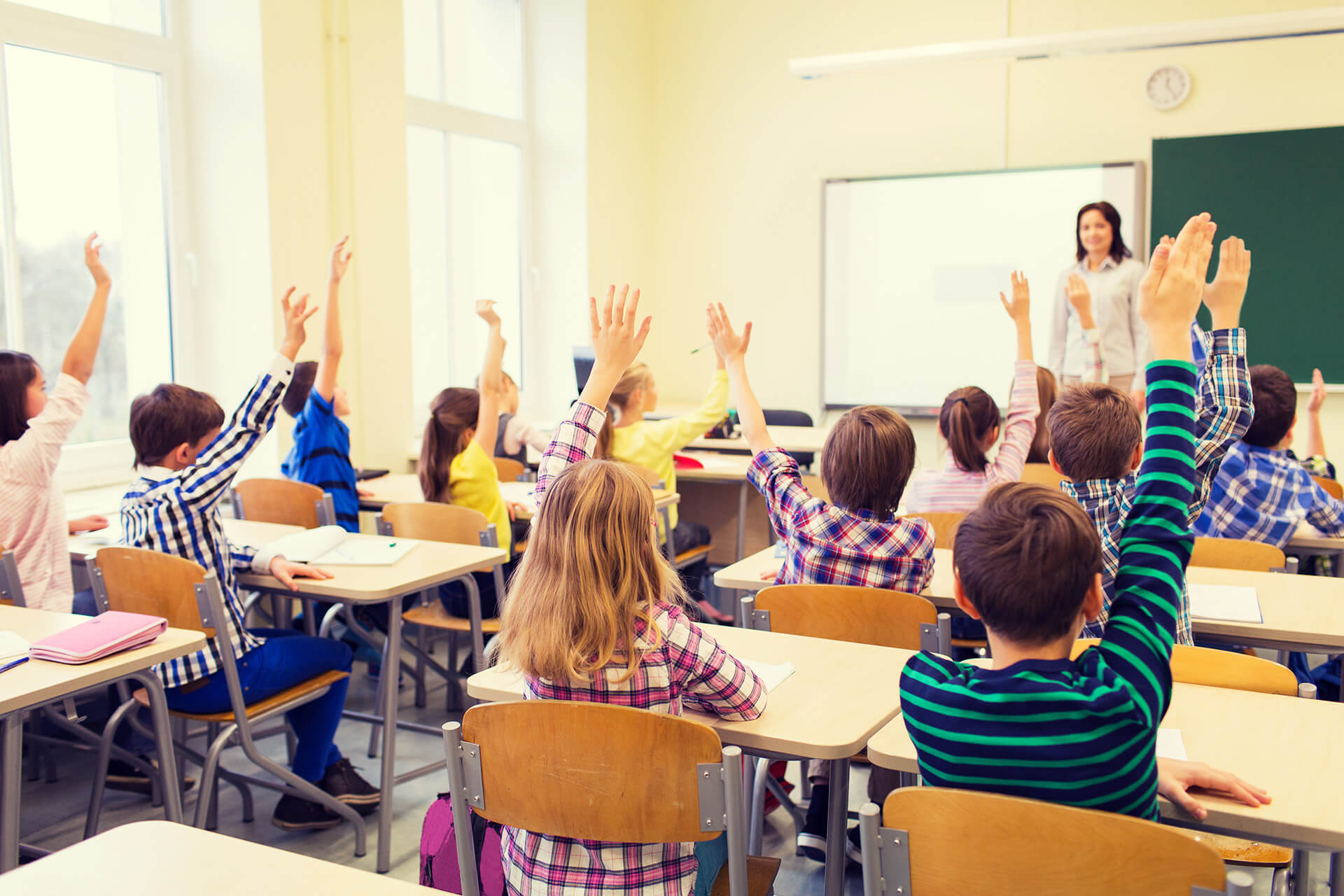 Elementary students raising hand in class.