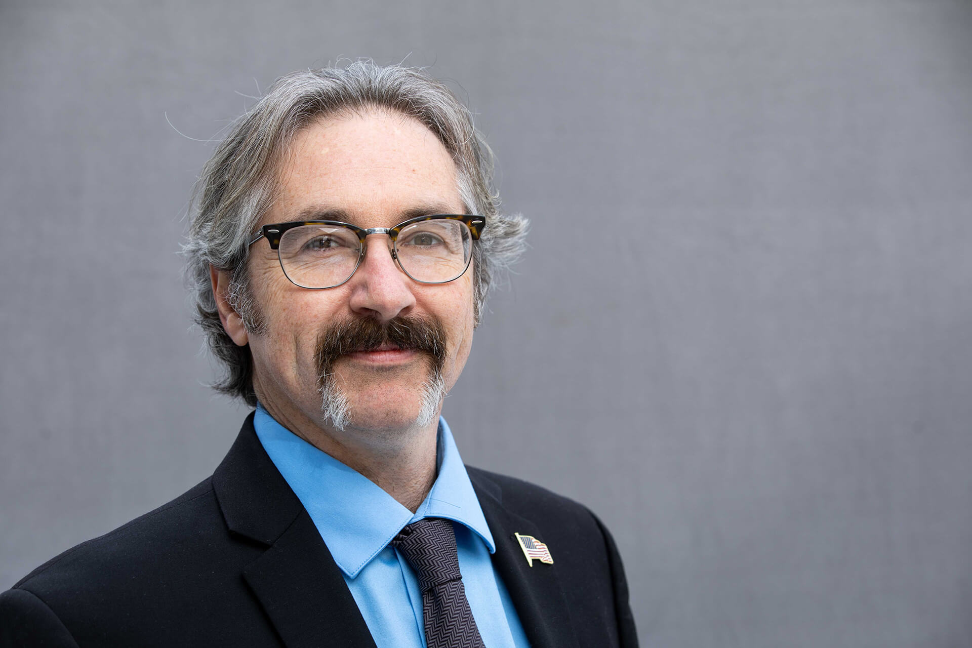 Joel O'Dorisio wearing blue dress shirt, suit jacket, and flag pin.